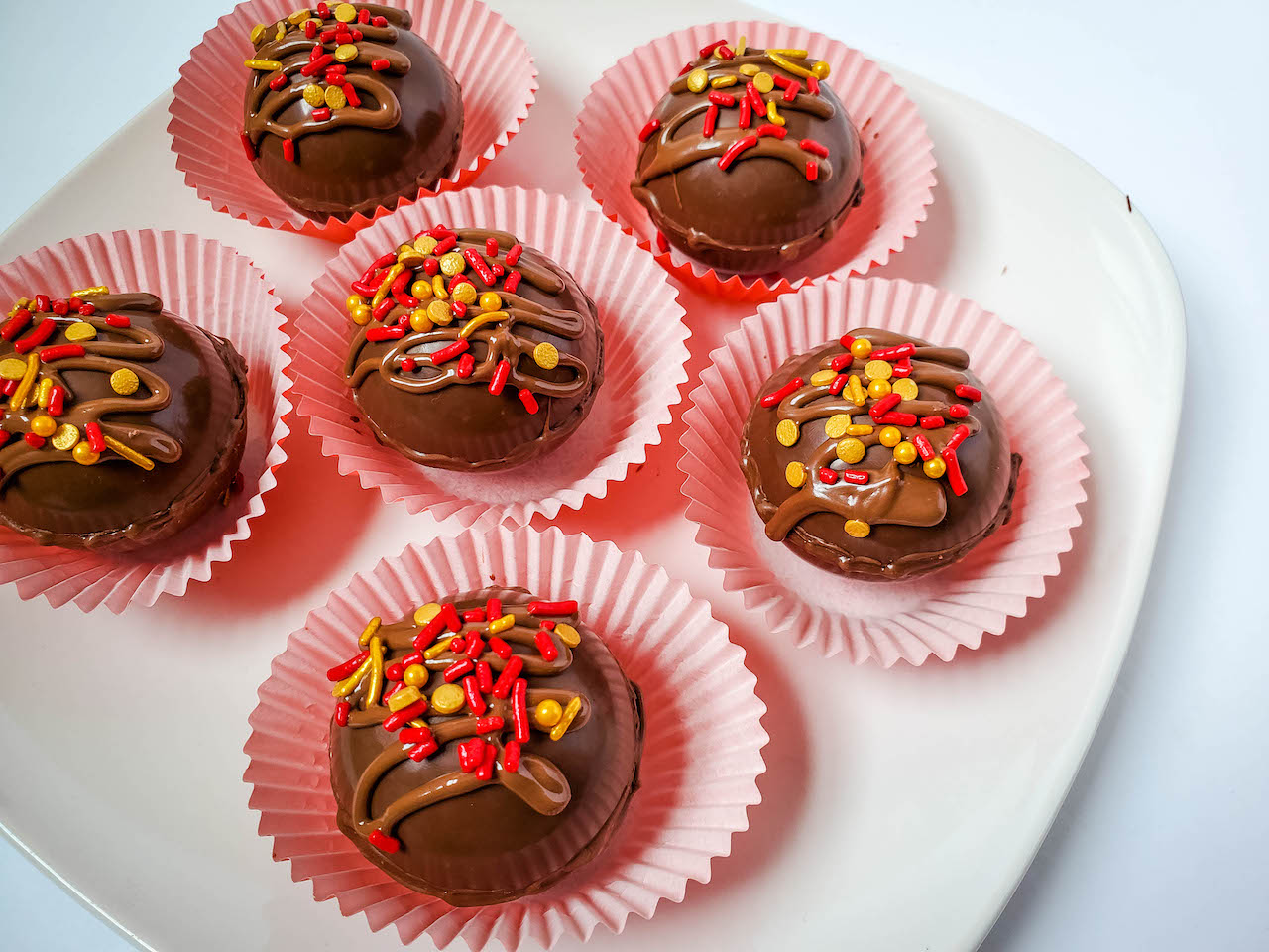 six hot chocolate bombs sitting in cupcake liners on top of a white plate