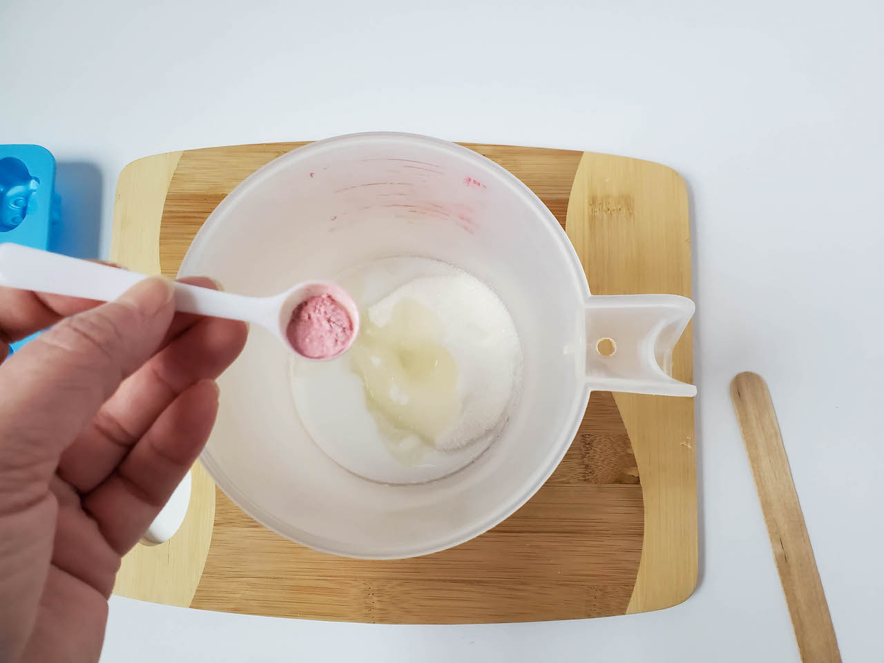 pink mica powder being added to measuring cup with soap, oil, and sugar