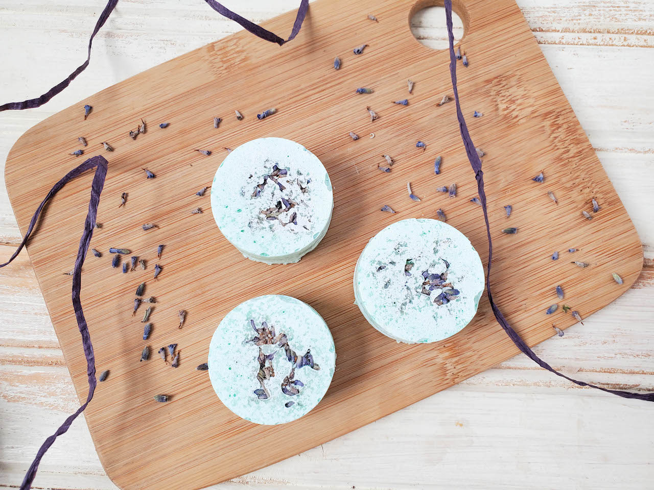 three diy shower steamers sitting on a wood board with tea tree leaves surrounding