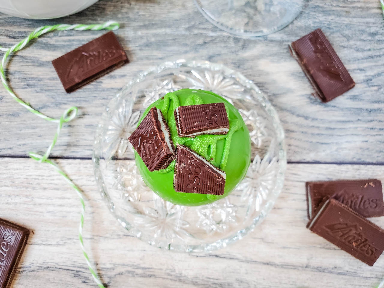 one andes mint hot chocolate bomb sitting on a glass plate surrounded by Andes mint candies