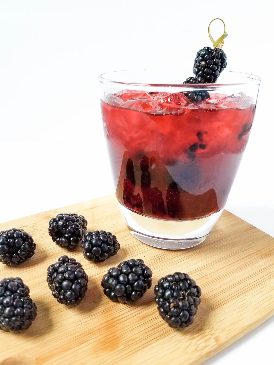 glass of blackberry margarita garnished with fresh blackberries sitting on a wooden board with additional fresh blackberries