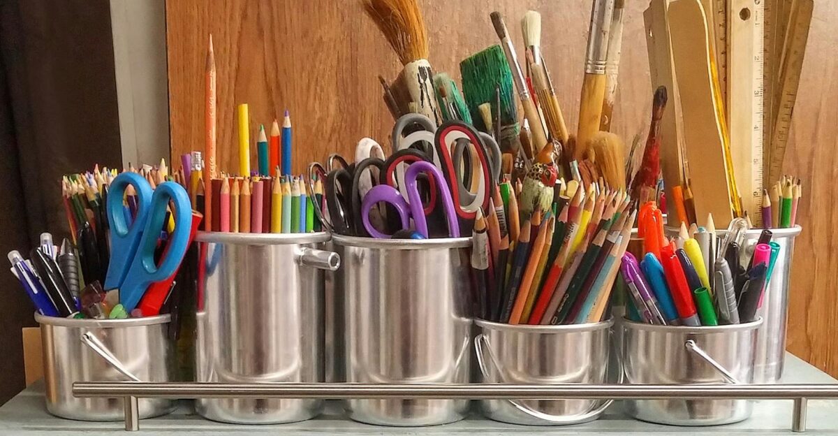 A diverse collection of art supplies in metallic buckets on a wooden table