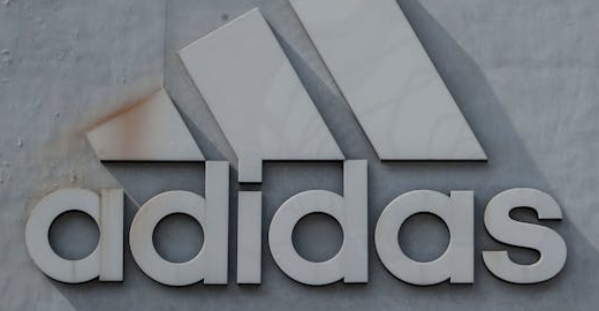 A father and child stand by a large Adidas logo on a modern building facade.