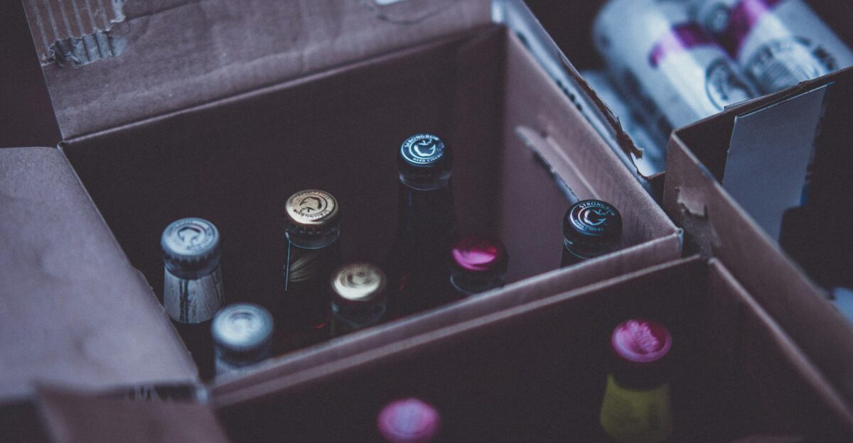 Close-up of various alcohol bottles and cans in cardboard boxes indoors.