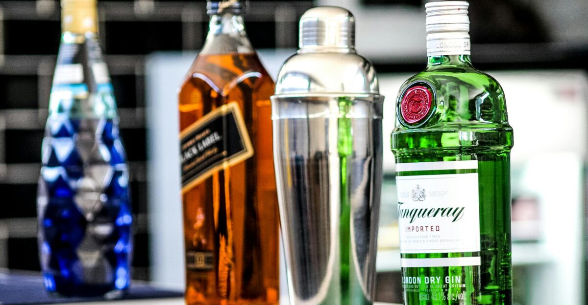 A selection of liquor bottles including gin, whiskey, and a cocktail shaker on display.