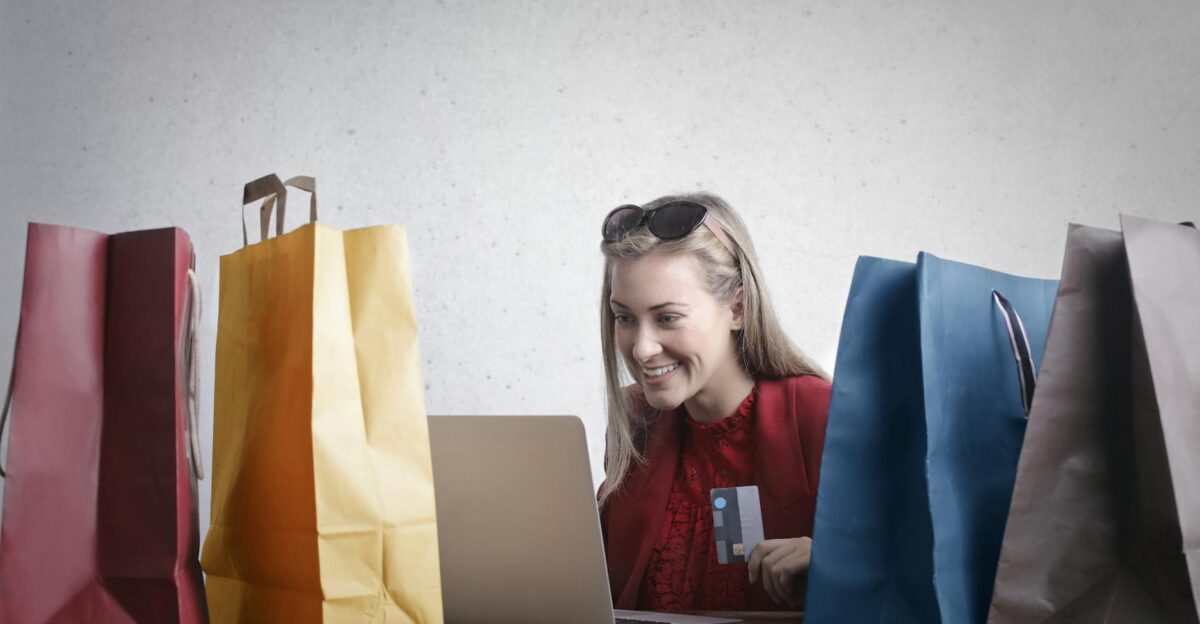 A joyful woman shopping online using a laptop with colorful shopping bags surrounding her