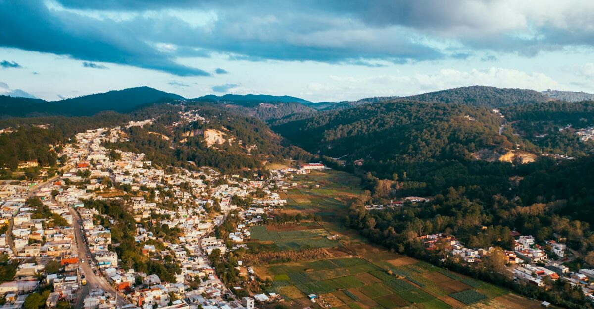 Aerial view capturing a rural town nestled against lush green mountains under dramatic skies