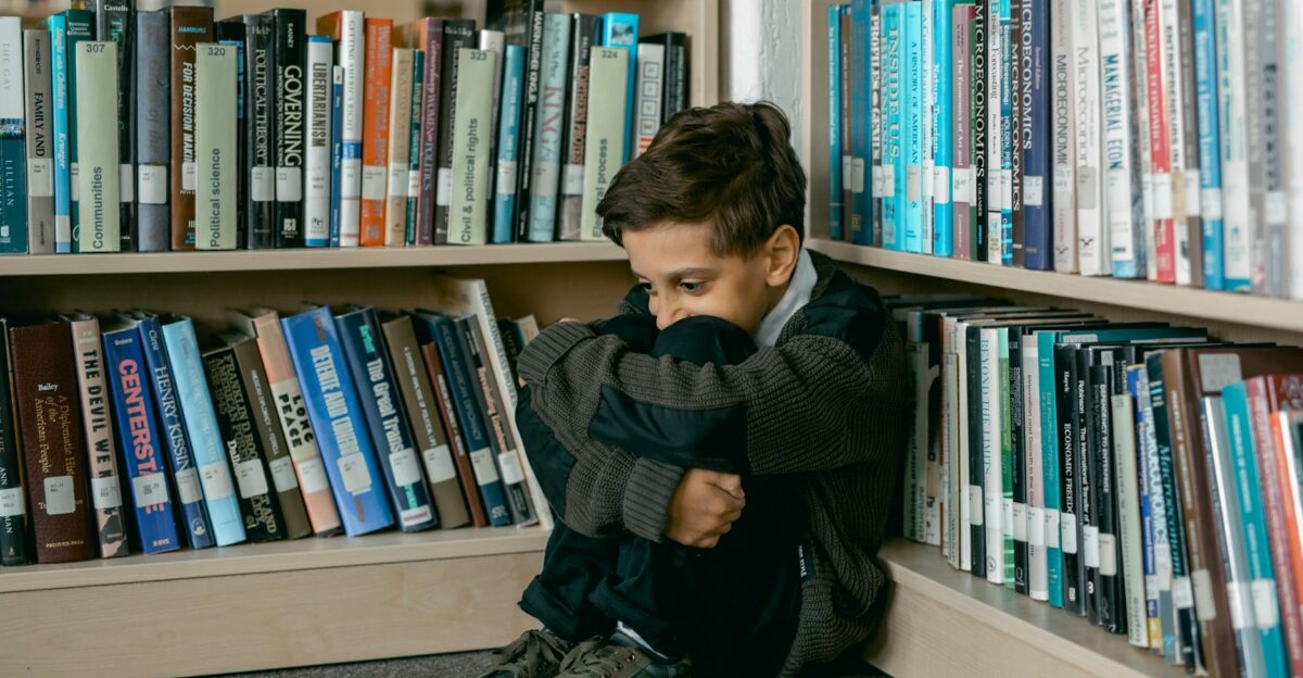 Young boy in library appears sad sitting alone among bookshelves suggesting themes of solitude and bullying