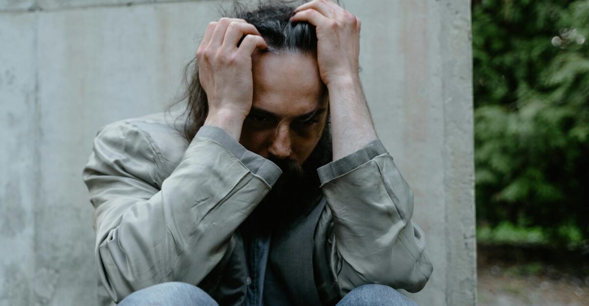 A pensive man sitting outdoors, expressing deep contemplation and emotional struggle.