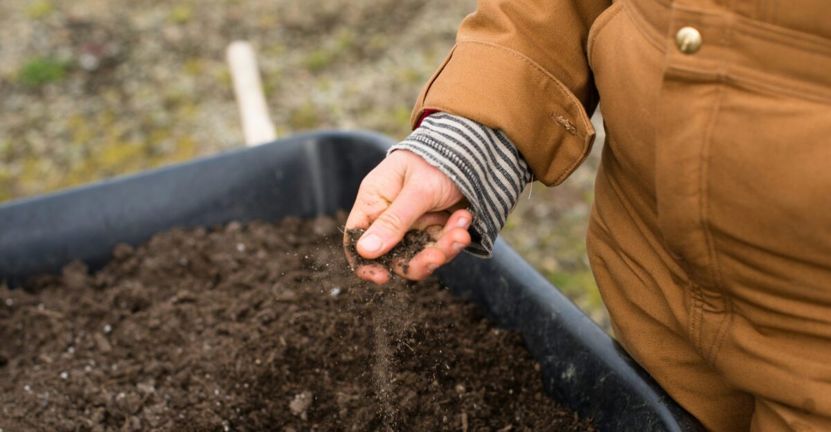 person in yellow jacket holding black soil
