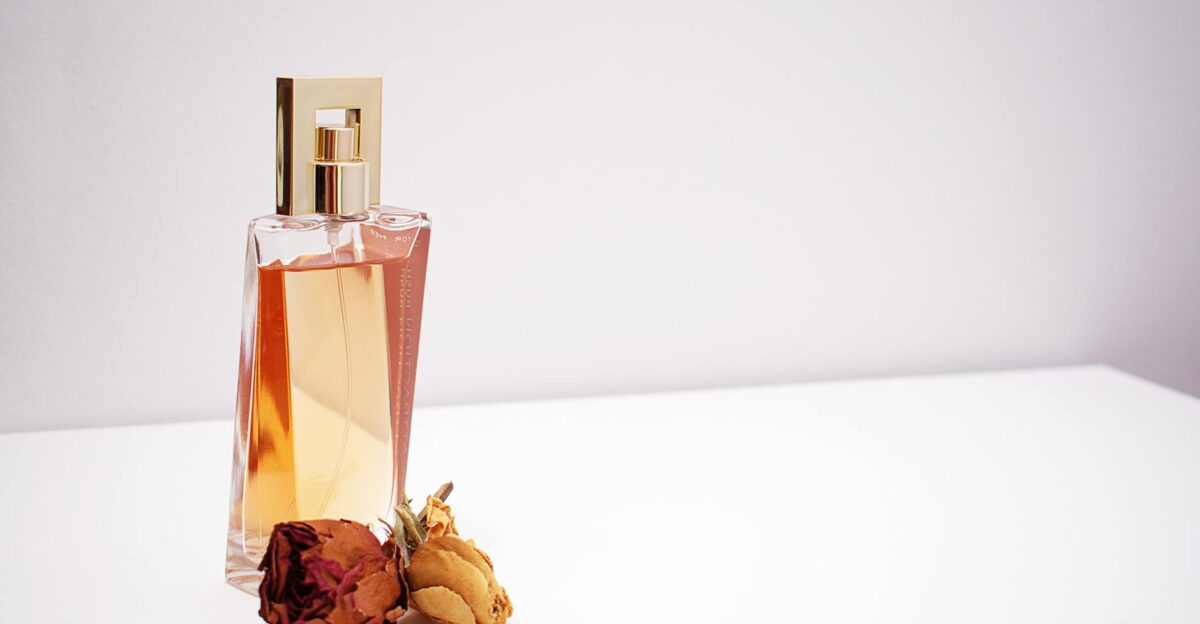 Elegant glass perfume bottle with luxurious design placed next to dried flowers against a minimalistic white background