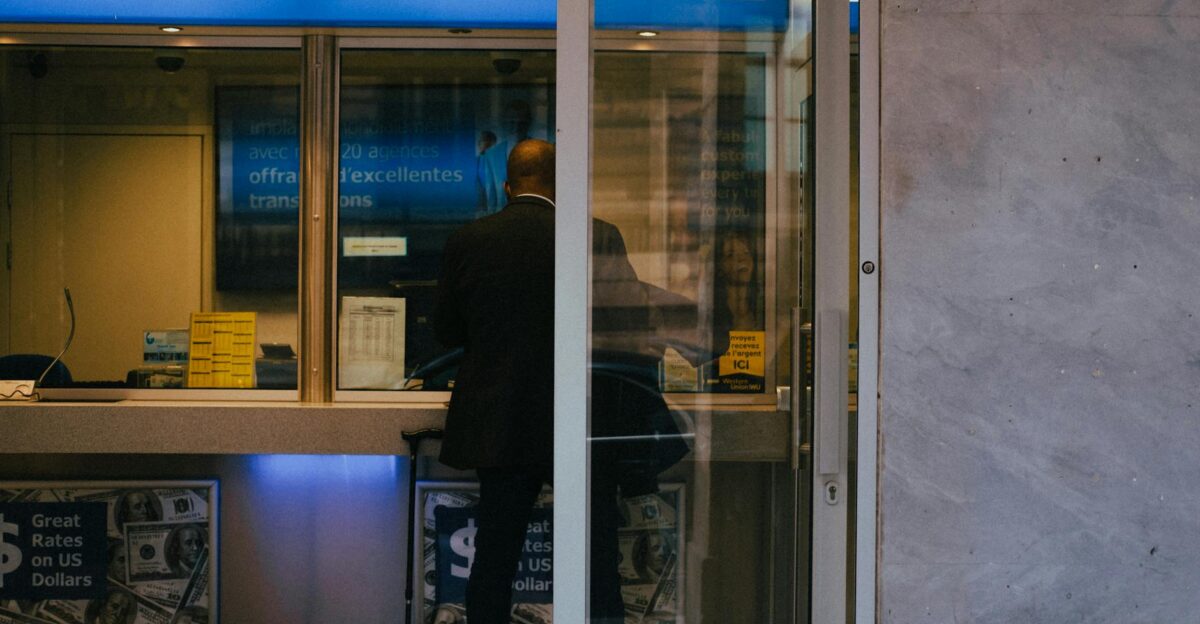Man at a currency exchange office window showing currency rates inside a bustling city