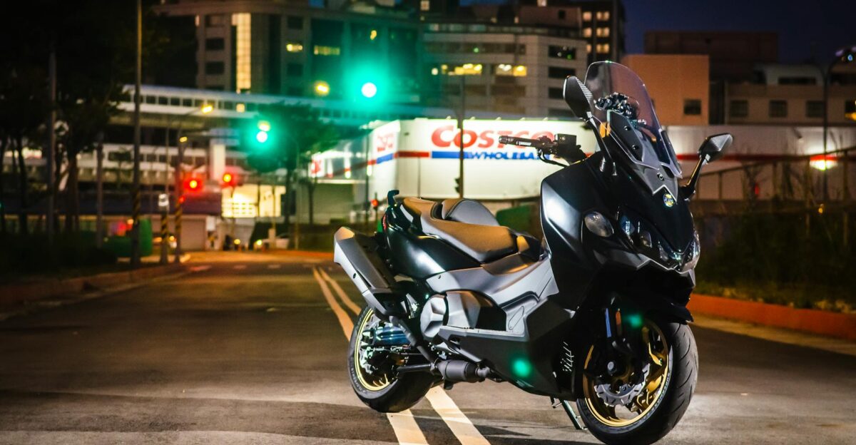 A sleek black motorcycle parked on a city street at night illuminated by vibrant lights