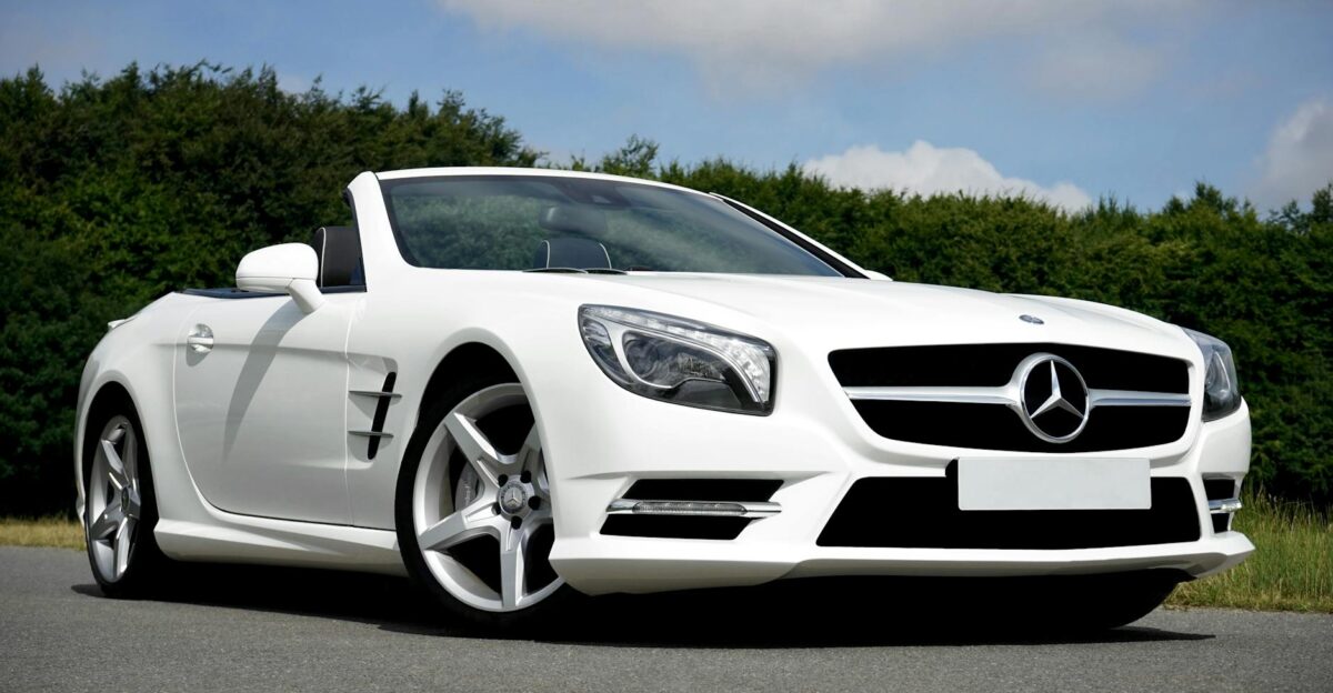Stunning white Mercedes Benz convertible parked on the road against a lush green backdrop