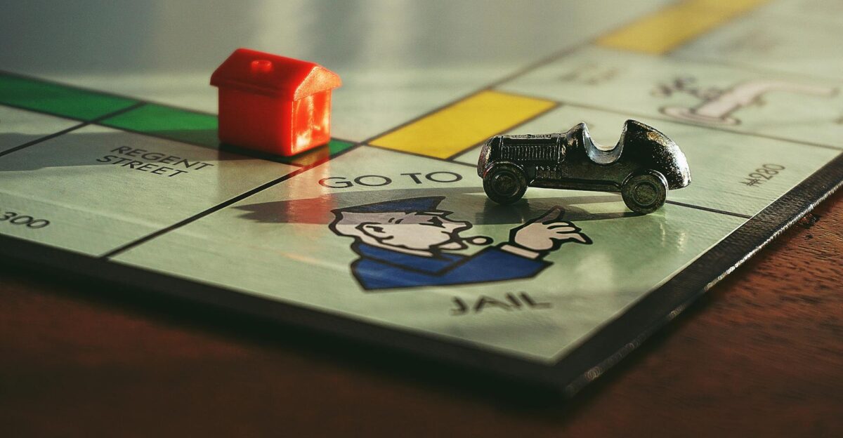 Close-up shot of a Monopoly board game featuring a toy car and a red house on Go to Jail