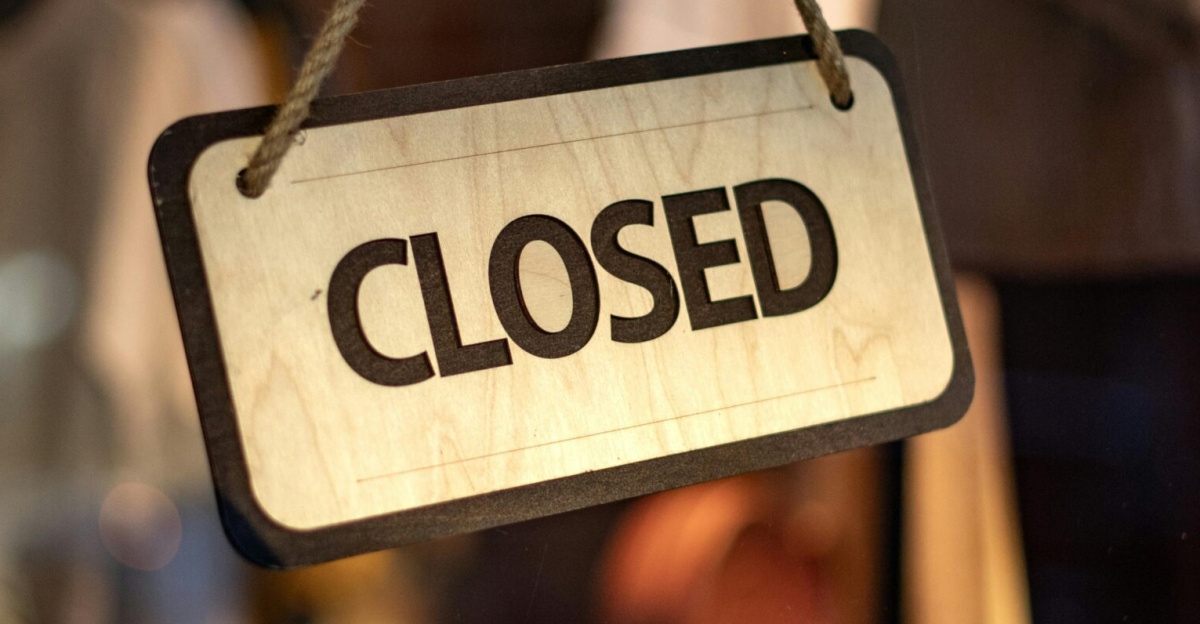 A wooden closed sign hanging on a storefront window at night.