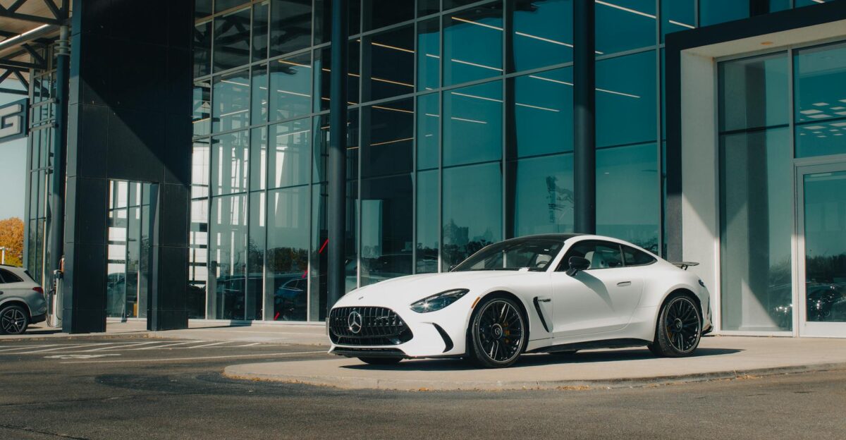 White Mercedes-Benz AMG displayed outside a modern dealership with glass walls on a sunny day