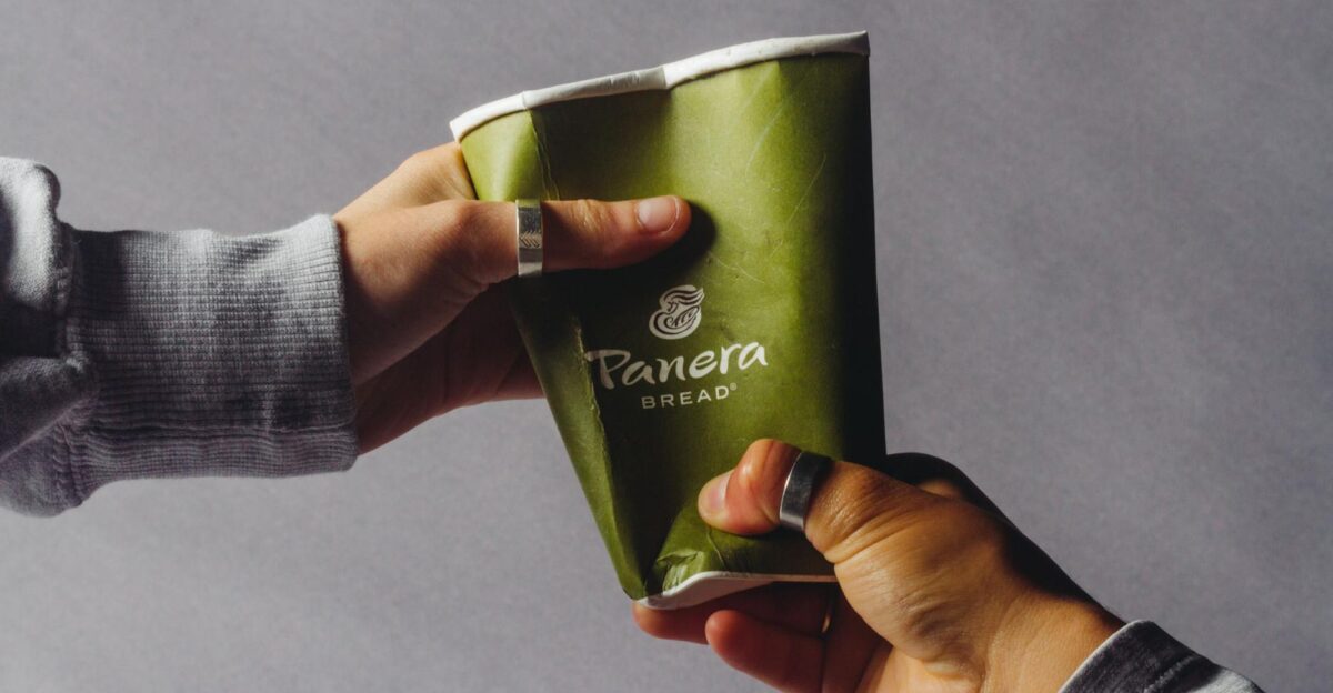 Close-up of two hands exchanging a crushed green disposable coffee cup indoors