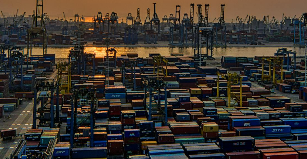 Sunset over a bustling seaport filled with stacked shipping containers and cranes