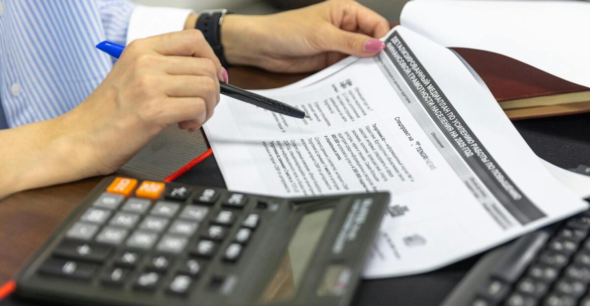 Close-up of a person analyzing financial documents using a calculator and pen