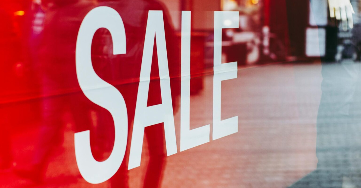 Red sale sign on storefront window reflecting a busy urban street scene, capturing city life.