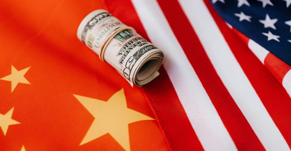 A rolled US dollar placed on overlapping USA and China flags symbolizing international trade relations