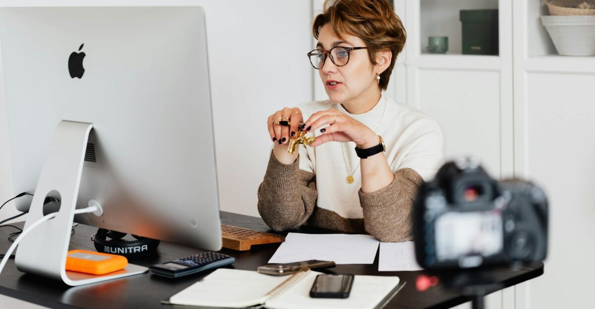 A professional woman engaged in a virtual meeting setup at her home desk using a computer and camera