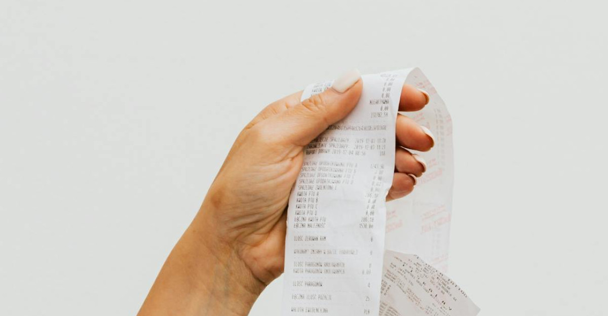 A detailed view of a person holding a long shopping receipt against a plain background