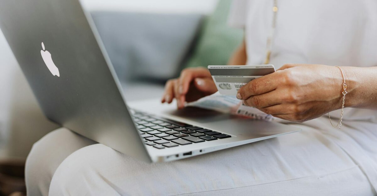 Close-up of a person holding a credit card while shopping online using a laptop at home