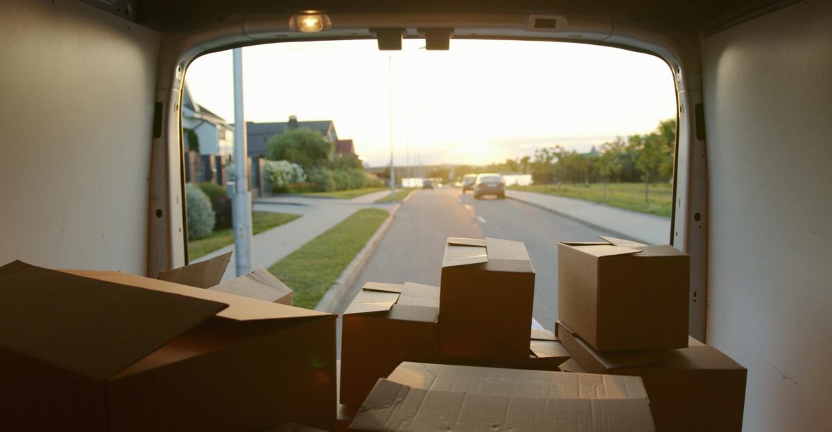 A scenic view from a delivery van loaded with cardboard boxes at sunset on a suburban street