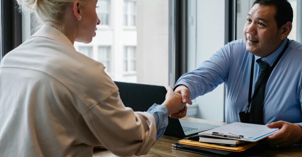 Two professionals in an office setting shaking hands after a business agreement