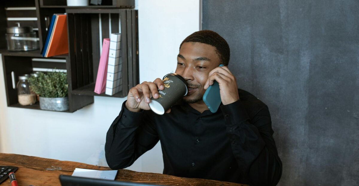 Confident businessman multitasking with phone call and coffee in stylish office
