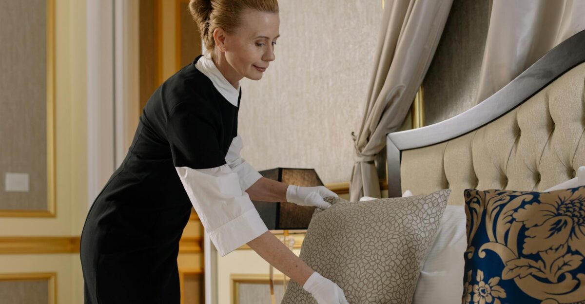 A housekeeper in uniform adjusts pillows in a luxurious hotel room ensuring comfort and cleanliness