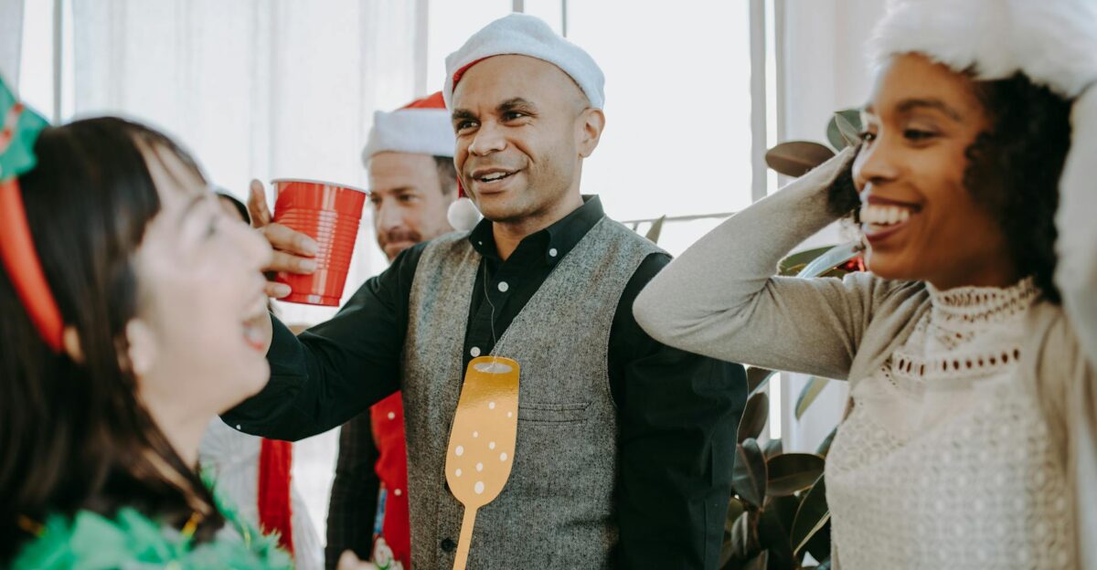 Group of colleagues enjoying a festive office party with drinks and holiday hats