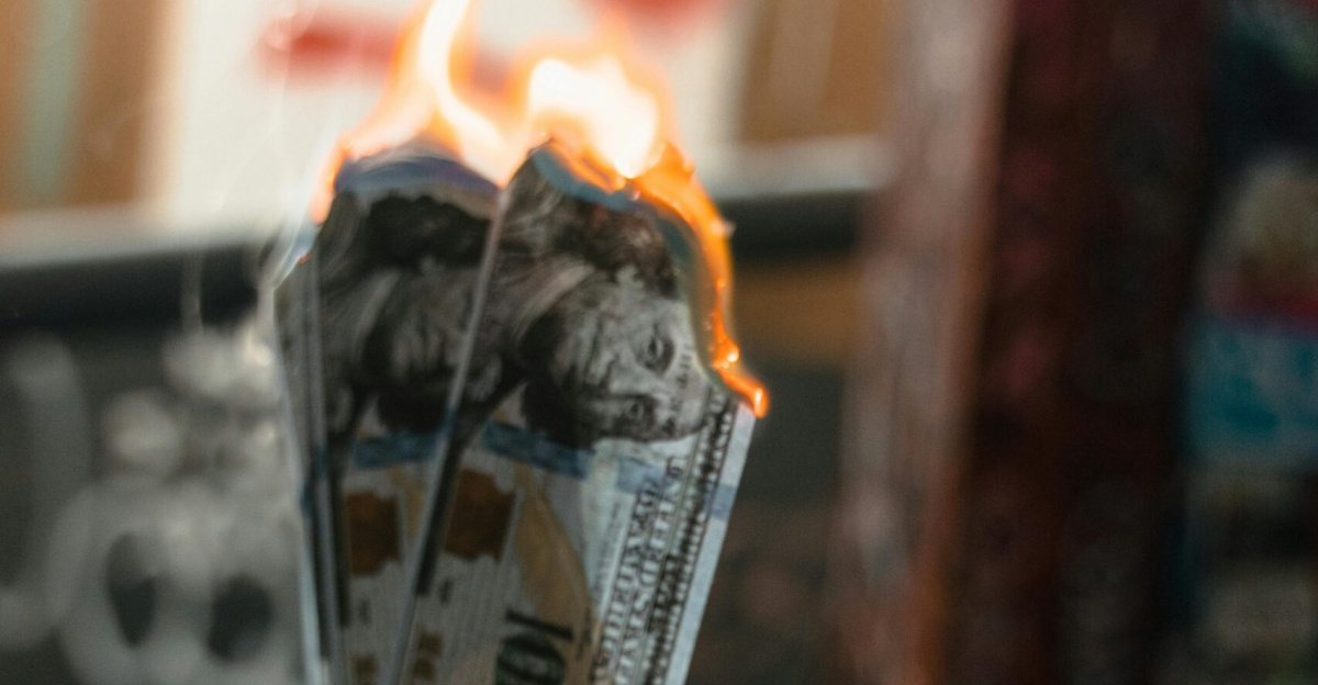 Dramatic image of burning dollar bills held against a graffiti-covered wall, symbolizing waste.