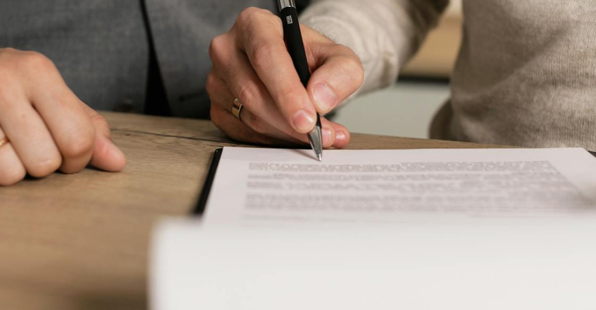 Close-up of businessmen signing documents at a wooden table in an office