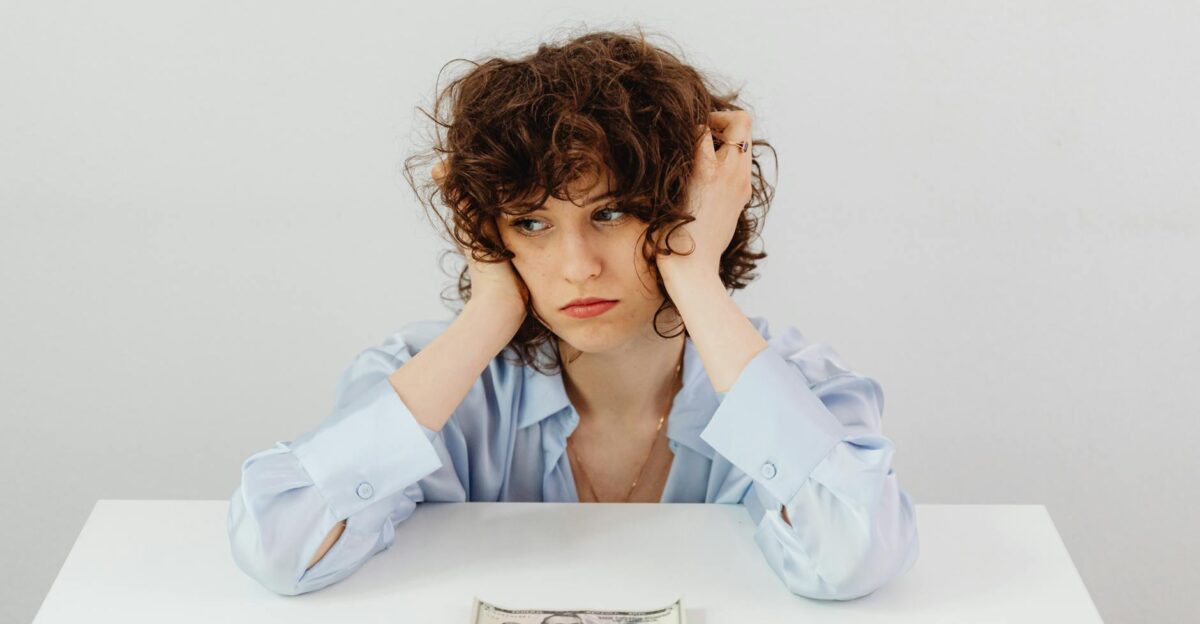 A woman in a blue blouse looks worried with a dollar bill on a table symbolizing financial stress