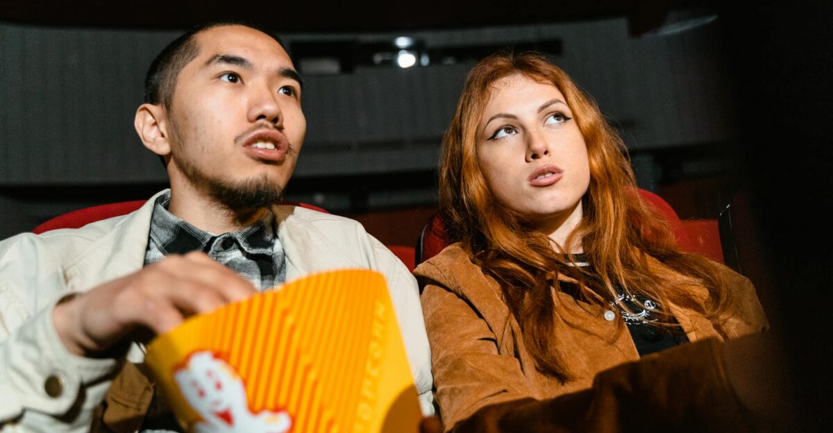 A couple sits in a movie theater engrossed in a film while enjoying popcorn