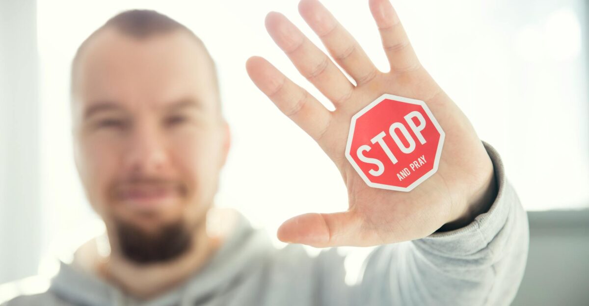 A man in a hoodie holds up his hand with a Stop and Pray sticker Focus on hand and sticker