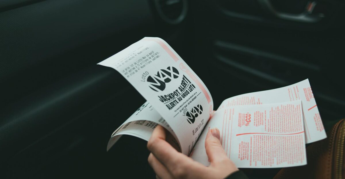 Close-up of hands holding Lotto Max papers inside a car symbolizing luck and chance