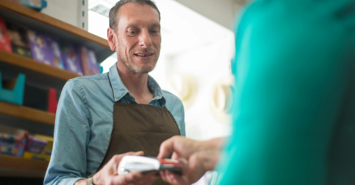 A male store clerk assisting a customer with a payment transaction in a retail shop setting