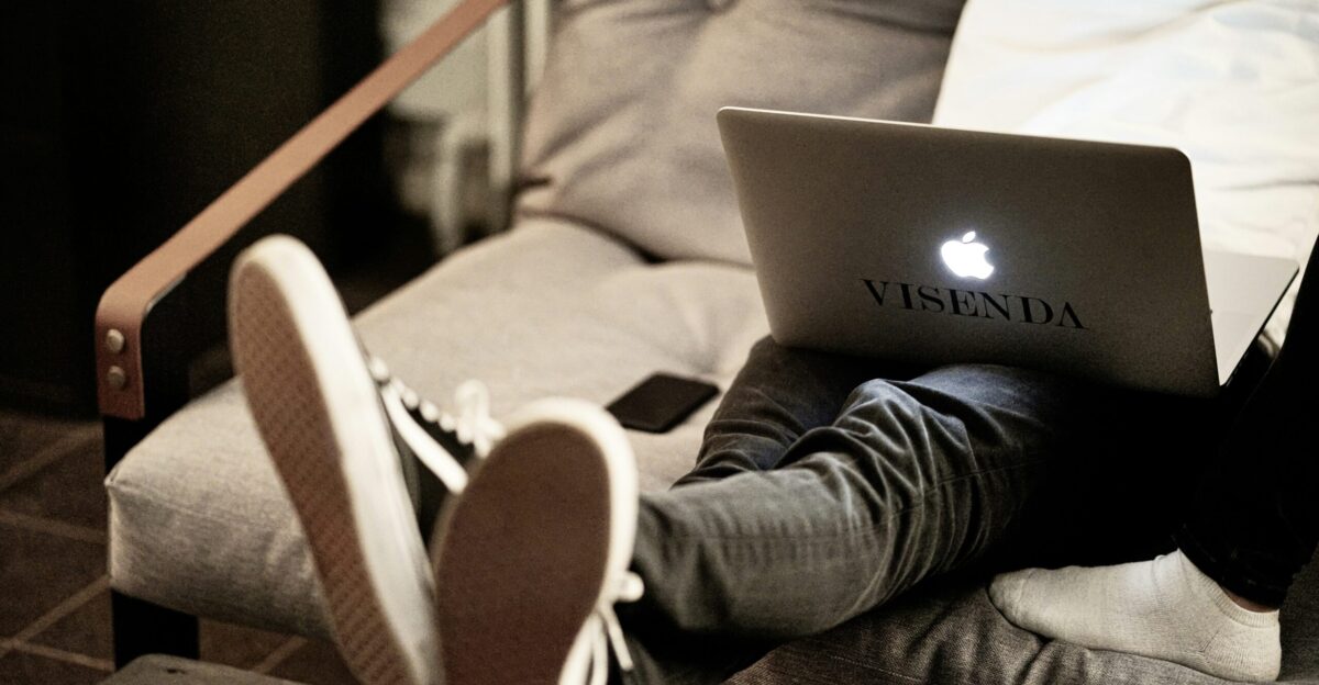 man in white long sleeve shirt and blue denim jeans sitting on brown sofa using macbook