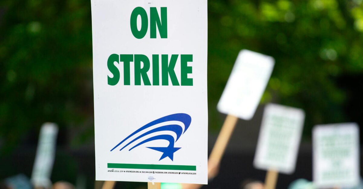 A protest sign with On Strike text held during an outdoor demonstration highlighting labor movements