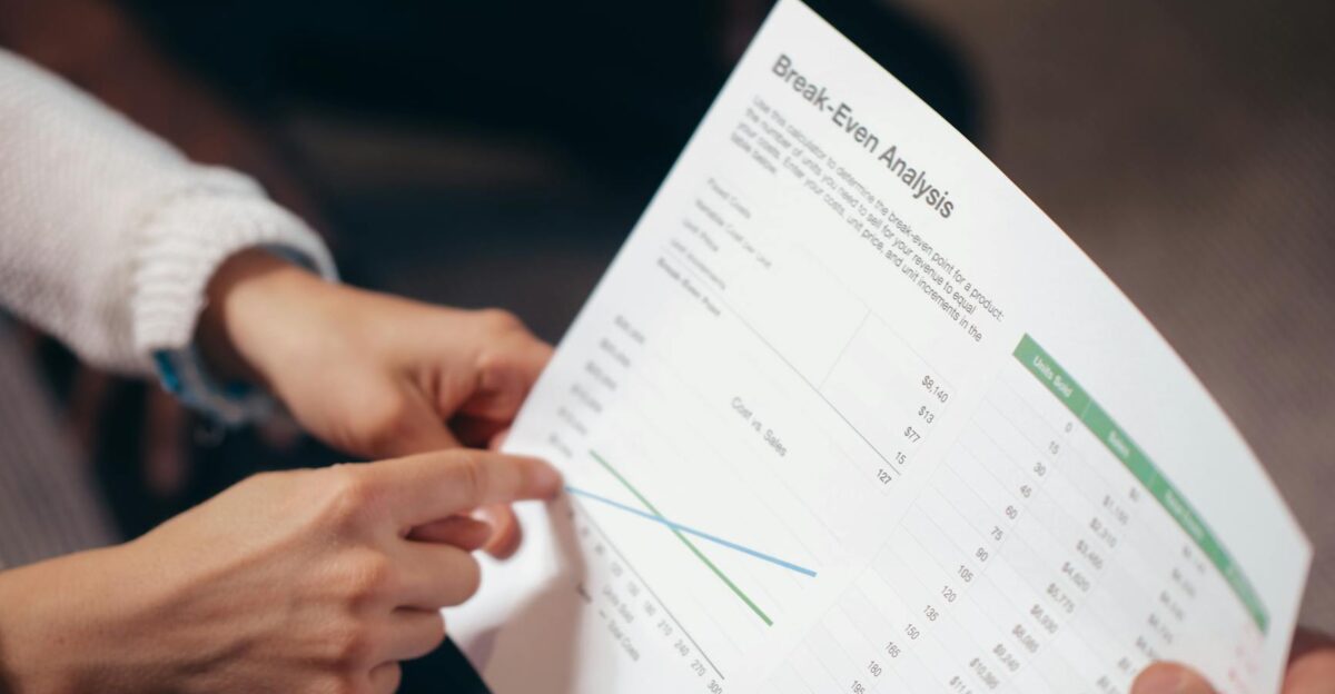 Close-up of hands discussing a break-even analysis document in a business meeting